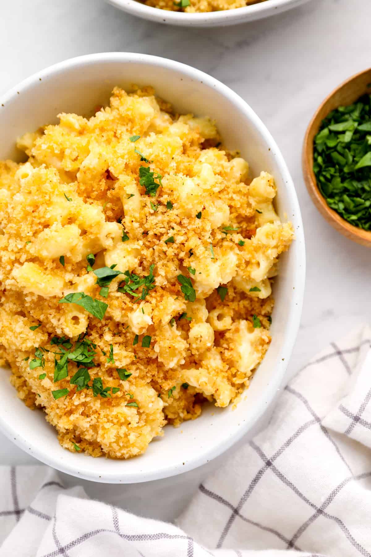 a serving of mac and cheese casserole in a white bowl with parsley.