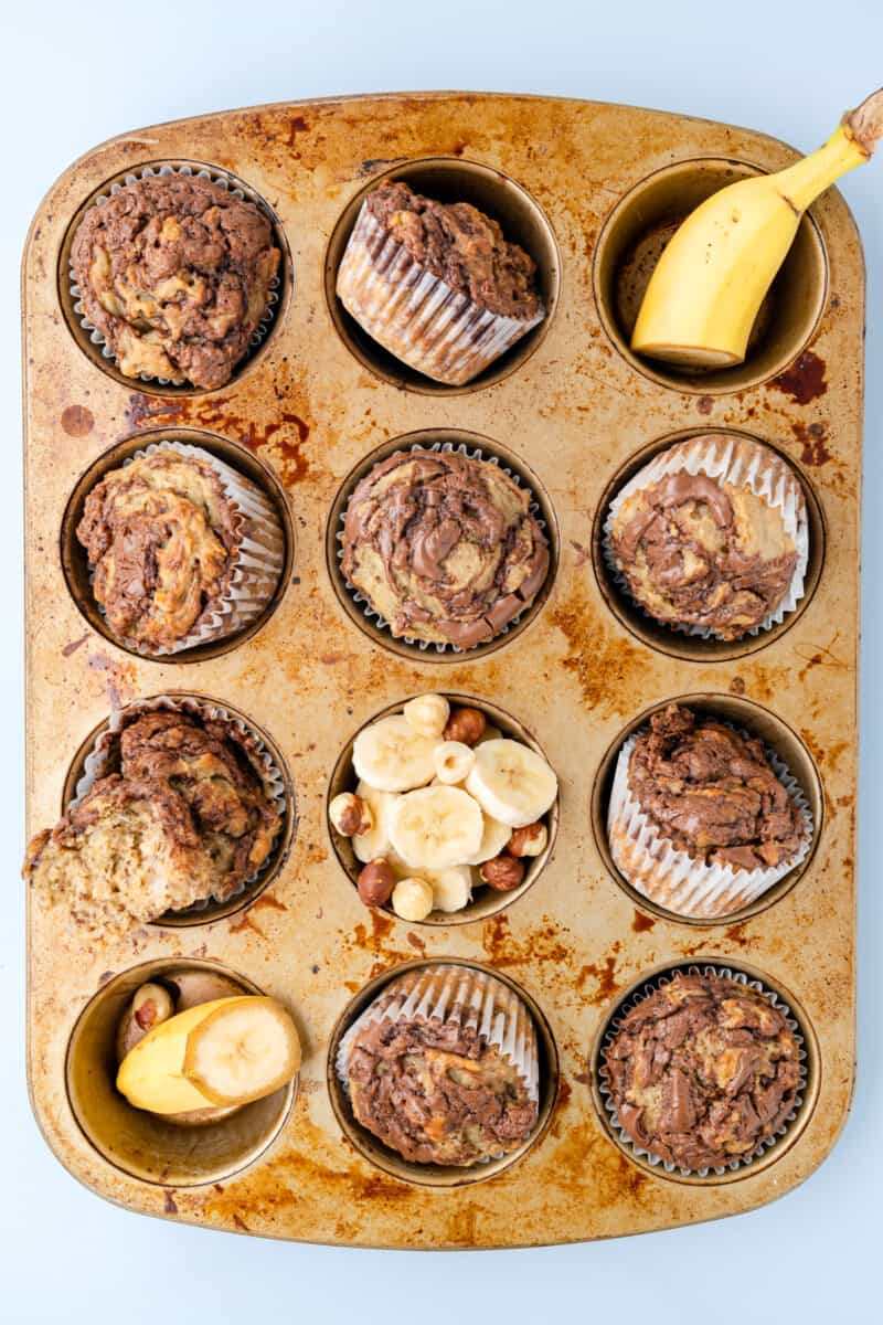vista dall'alto di muffin alla nutella di banana in una teglia per muffin con banane tagliate a metà e affettate.