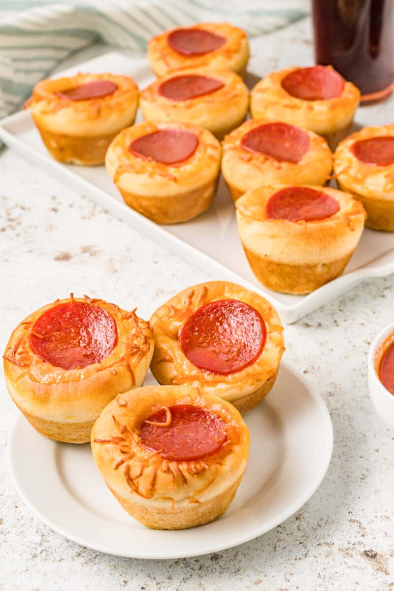 3 pizza cupcakes on a white plate with a tray of pizza cupcakes in the background.