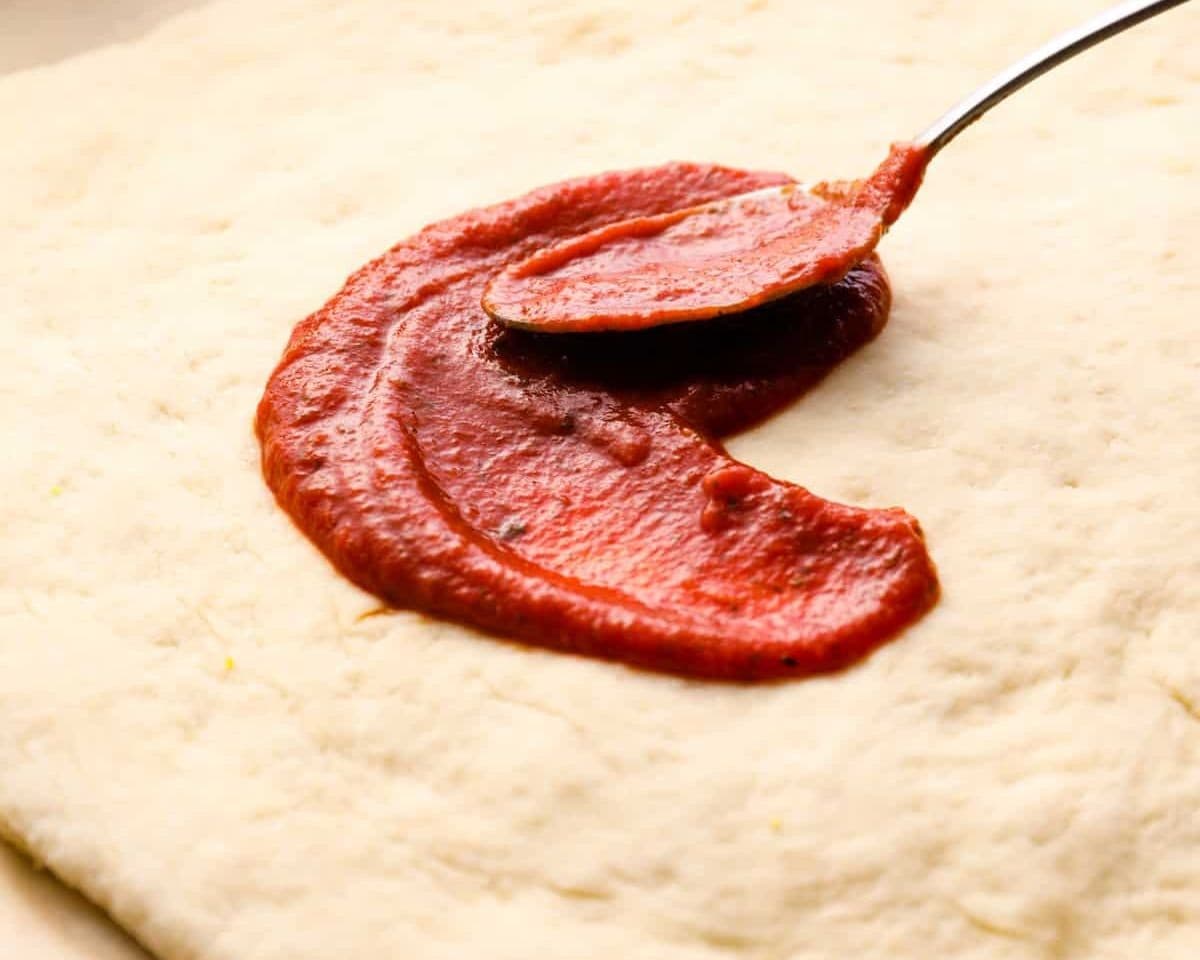 Spreading pizza sauce over the pizza dough. - 11