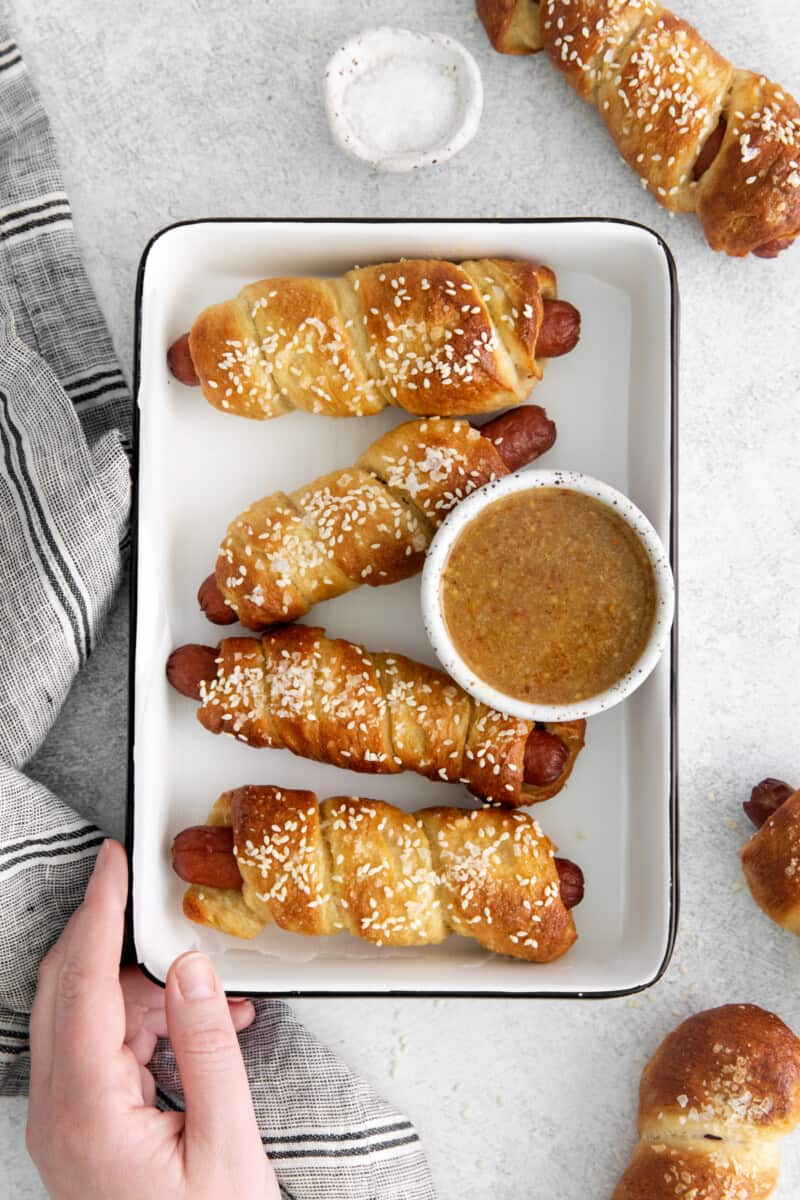 a tray of crispy pretzel dogs with a small bowl of dipping sauce