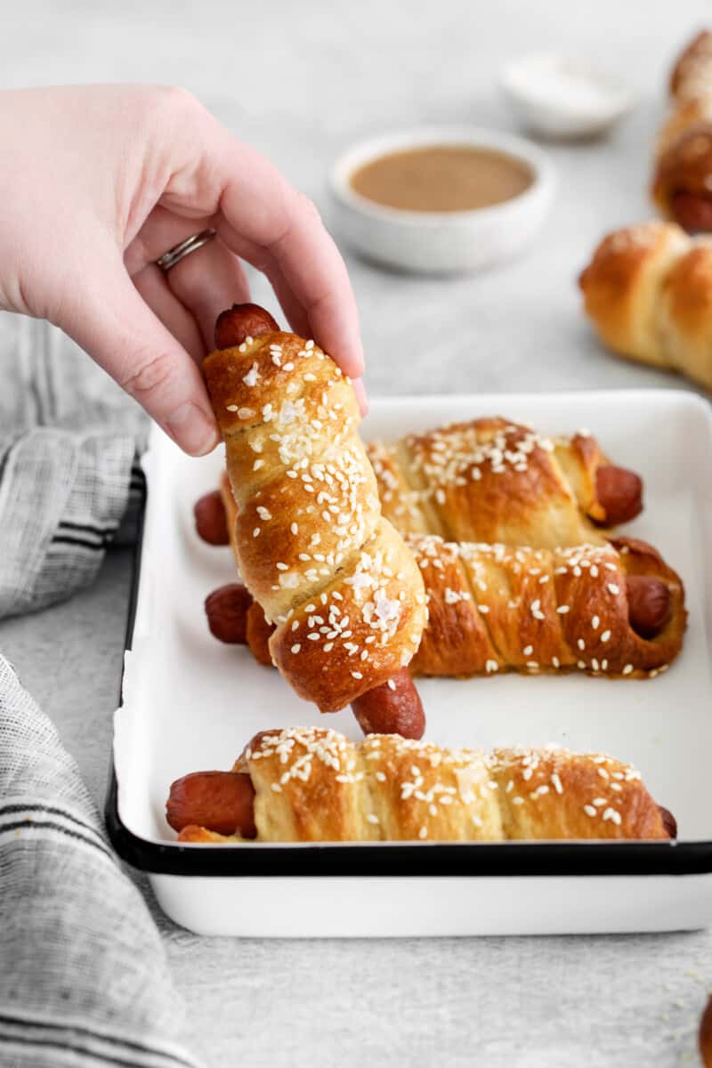 hand picking up one pretzel dog from a tray