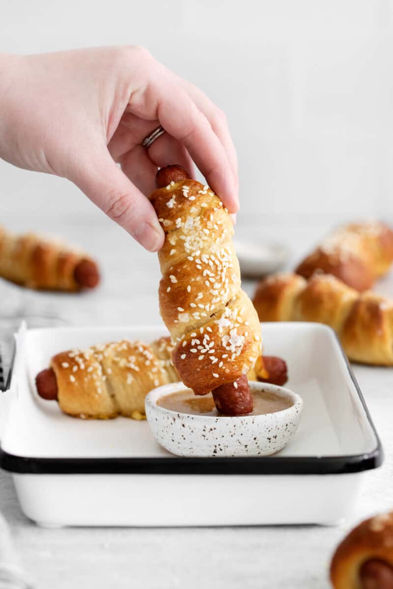 hand dipping a pretzel dog into a dip
