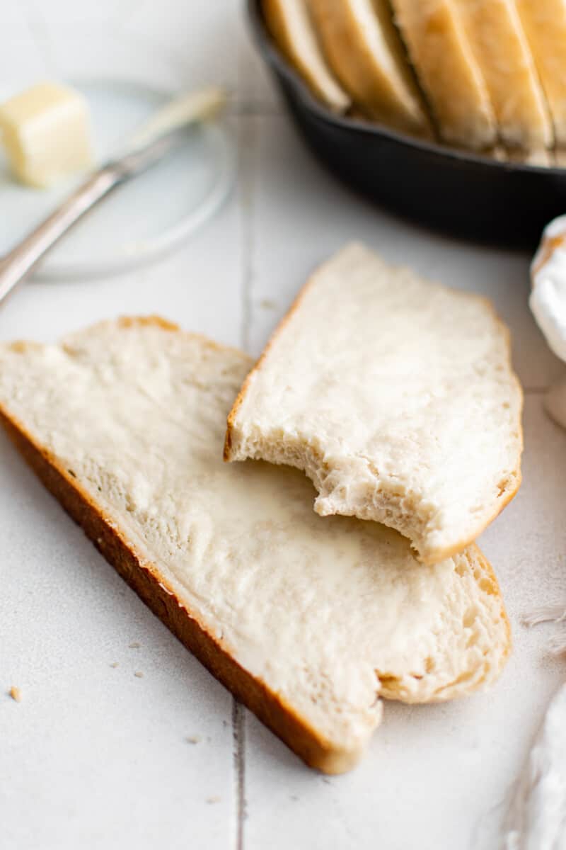 two slices of buttered bread on a countertop, one has bites taken out of it