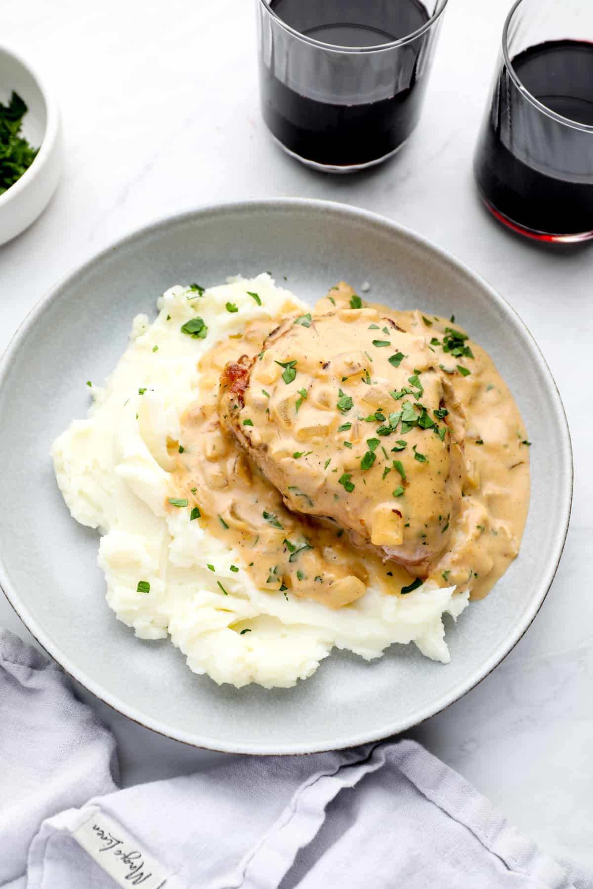 gravy smothered pork chops served on a dish with mashed potatoes and glasses of wine