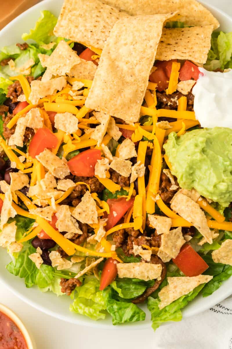 close up on taco salad, topped with crumbled tortilla strips, shredded cheese, and more