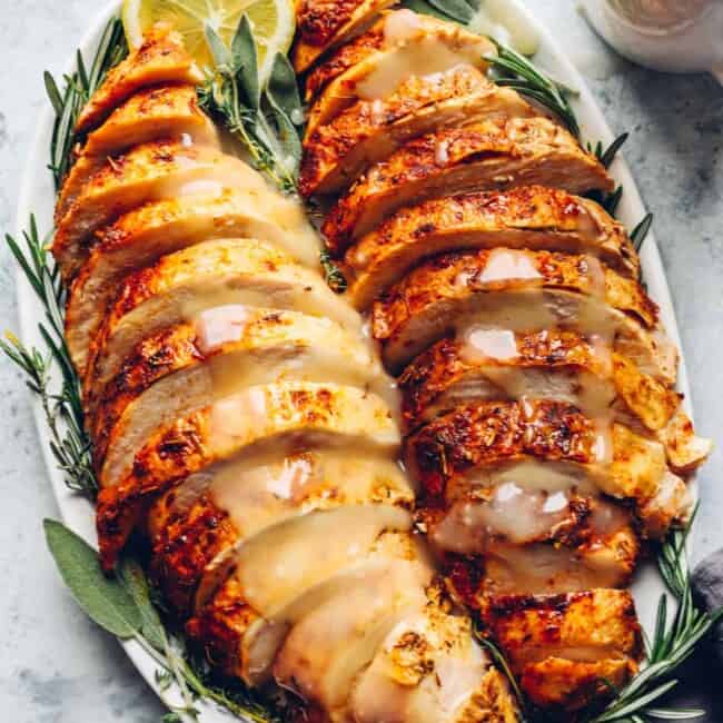 sliced thanksgiving turkey breasts on a white serving platter with lemons and herbs.
