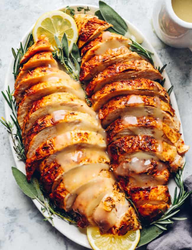 sliced thanksgiving turkey breasts on a white serving platter with lemons and herbs.