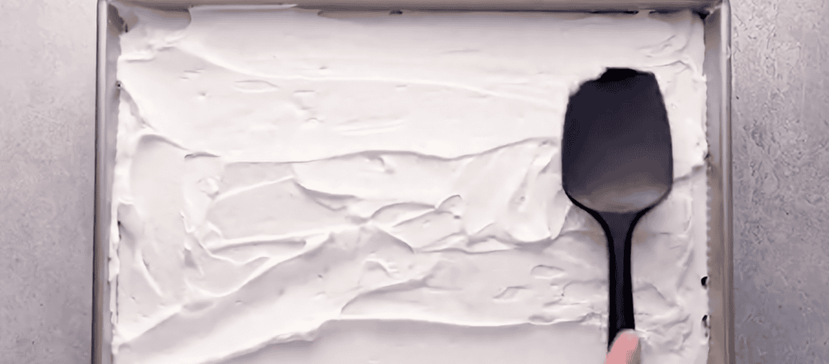 Spreading whipped cream topping over the cake.