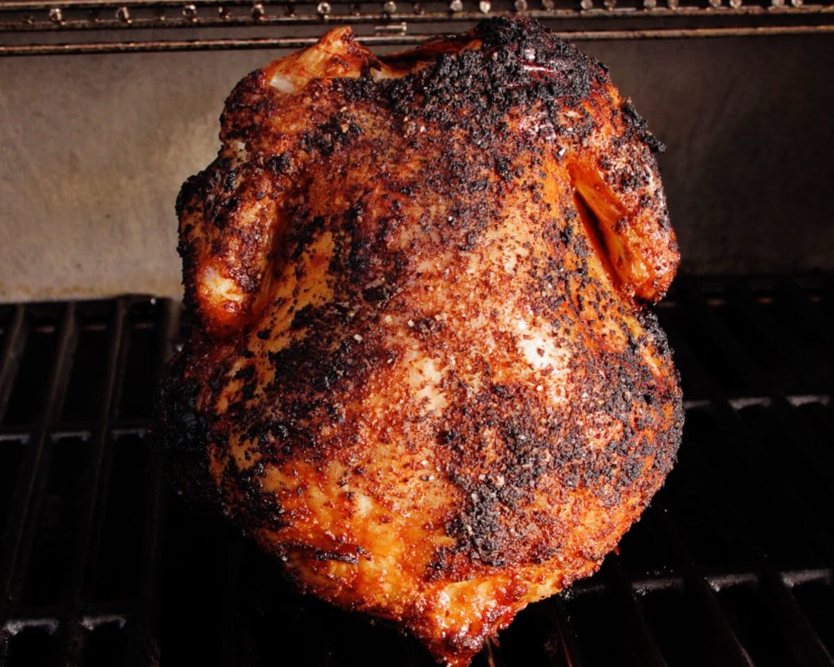 Close-up of seasoned beer can chicken on the grill with melted, drippy texture and crispy browned skin forming along the surface.