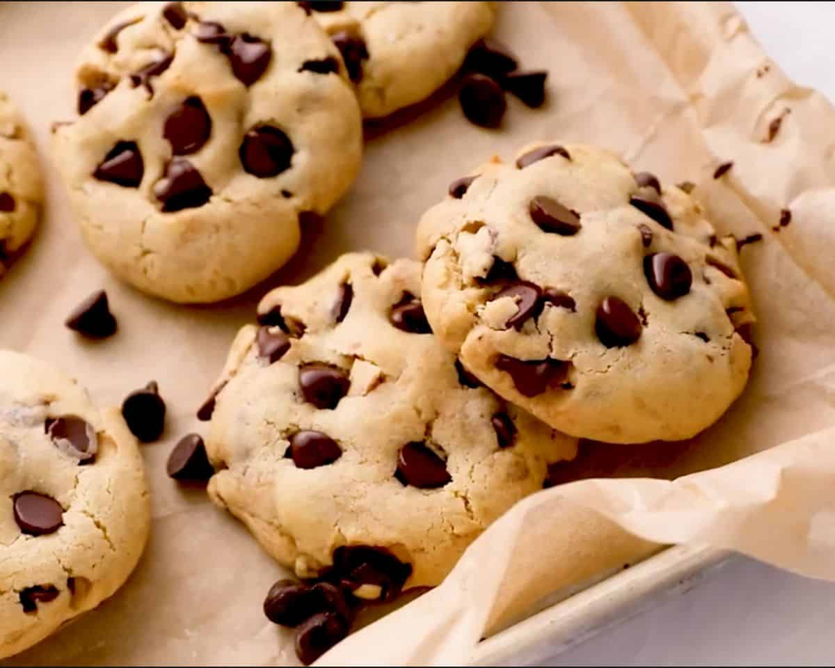 Chocolate chip cookies on a parchment-lined baking sheet, golden with soft centers and scattered melted chocolate chips on top and around the pan