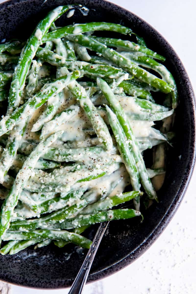 creamed green beans in black serving bowl with a spoon.