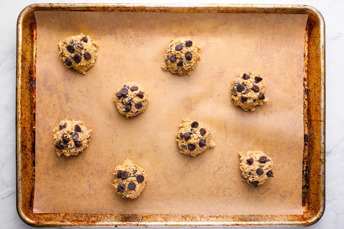 Scooped oatmeal chocolate chip cookie dough balls on parchment-lined baking sheet
