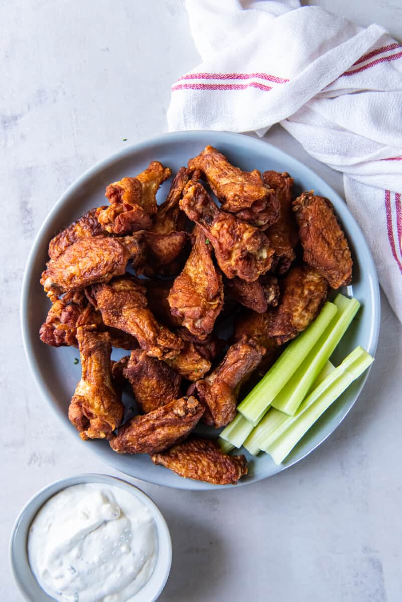 overhead view of trashed wings on a gray plate with celery sticks and ranch.