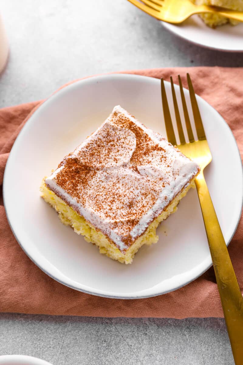 a slice of tres leches cake on a white plate with a gold fork.