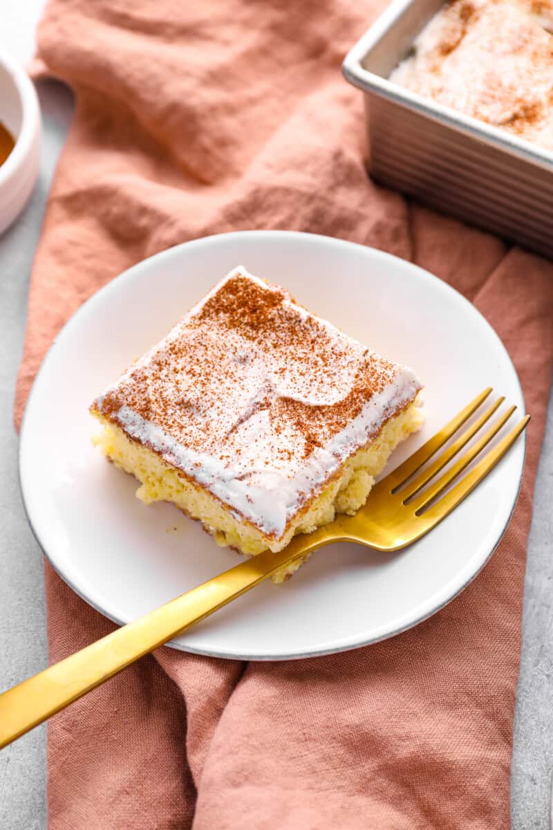 a slice of tres leches cake on a white plate with a gold fork.