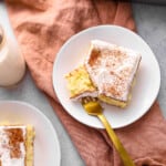 a forkful of tres leches cake resting on a white plate with a slice of tres leches cake.