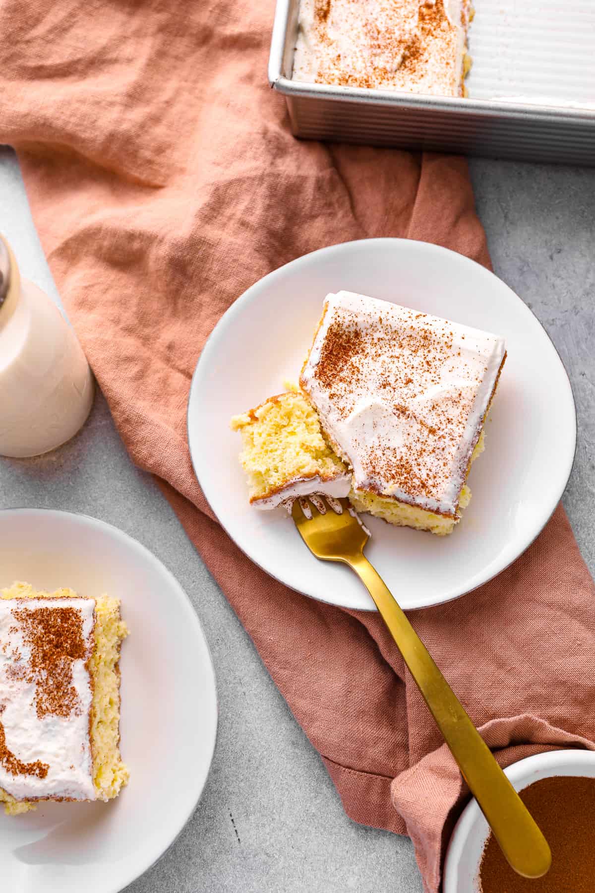 a forkful of tres leches cake resting on a white plate with a slice of tres leches cake.