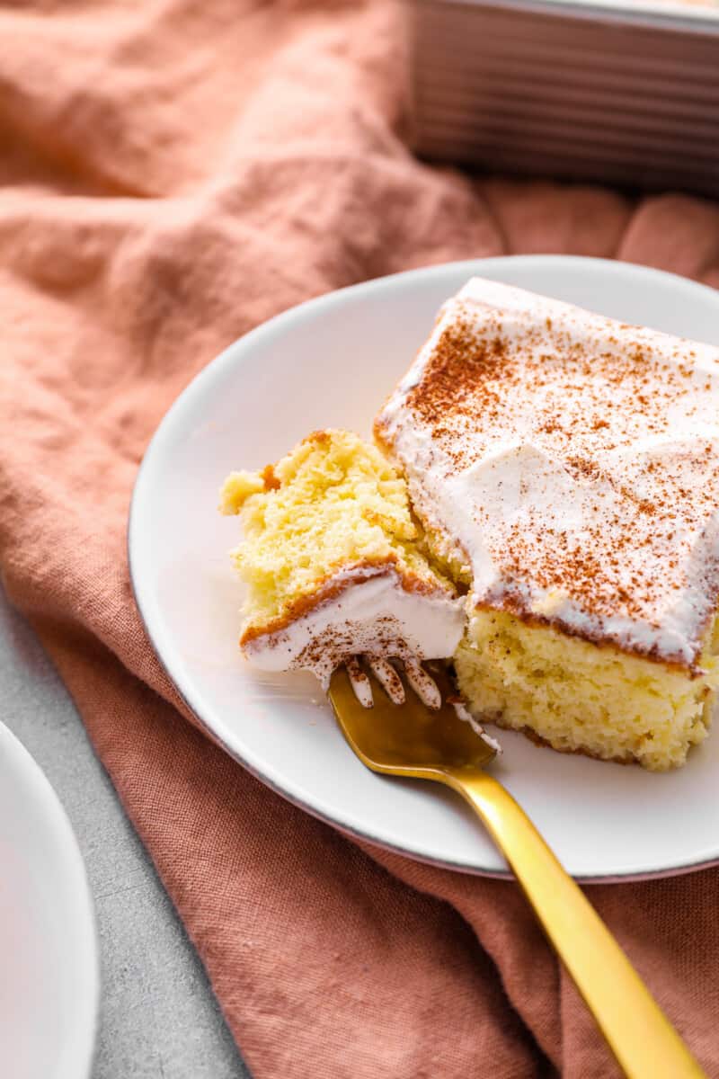 a forkful of tres leches cake resting on a white plate with a slice of tres leches cake.