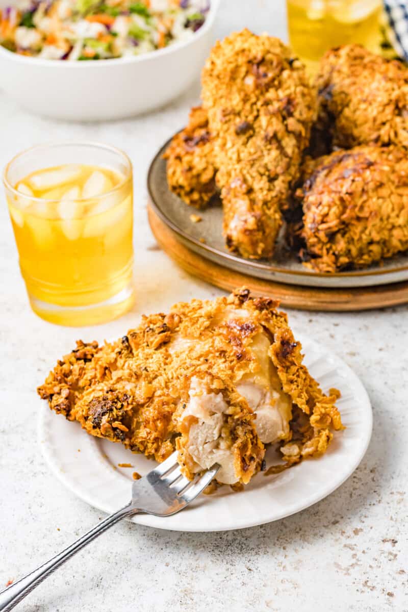 a forkful of air fryer fried chicken suspended above air fryer fried chicken on a white plate.