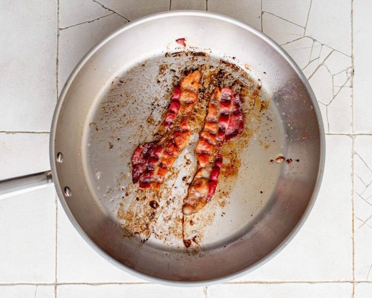 Two slices of bacon cooking in a pan.  - 7