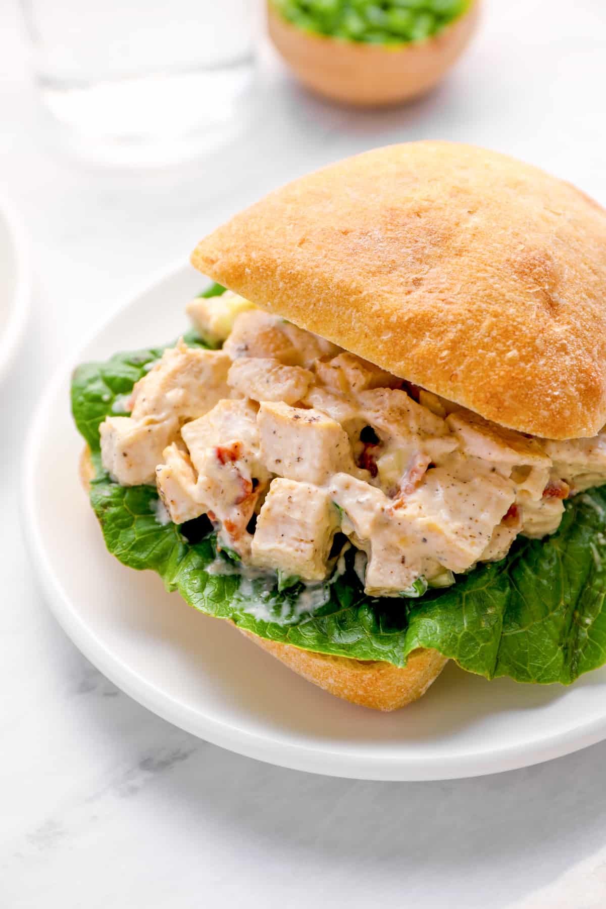 a bacon ranch chicken salad sandwich on a white plate.