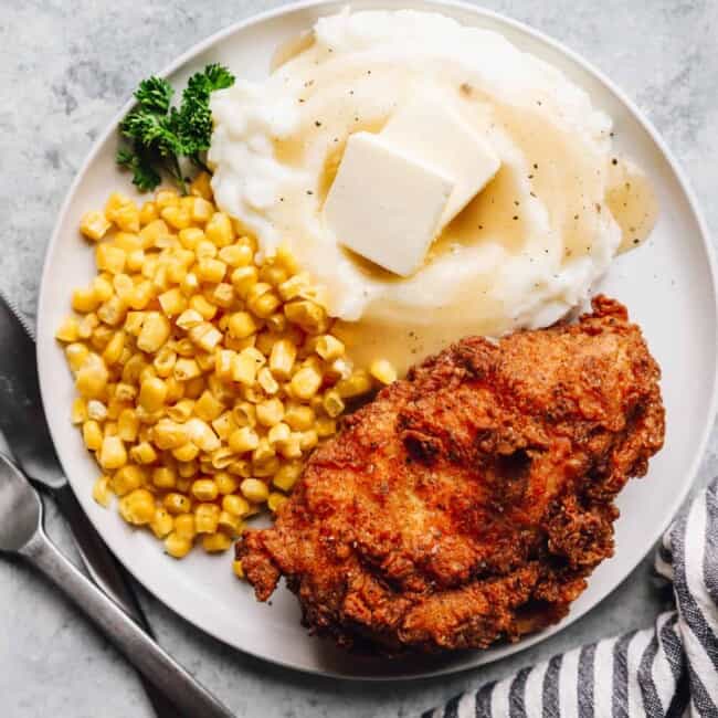 overhead view of a piece of kentucky fried chicken on a white plate with corn and mashed potatoes.