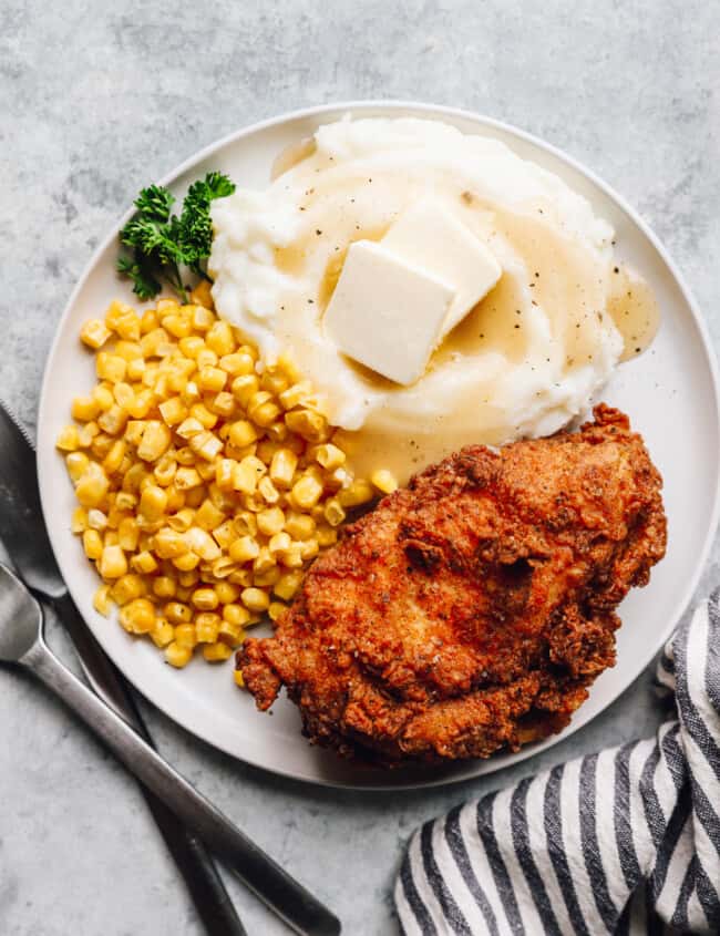overhead view of a piece of kentucky fried chicken on a white plate with corn and mashed potatoes.
