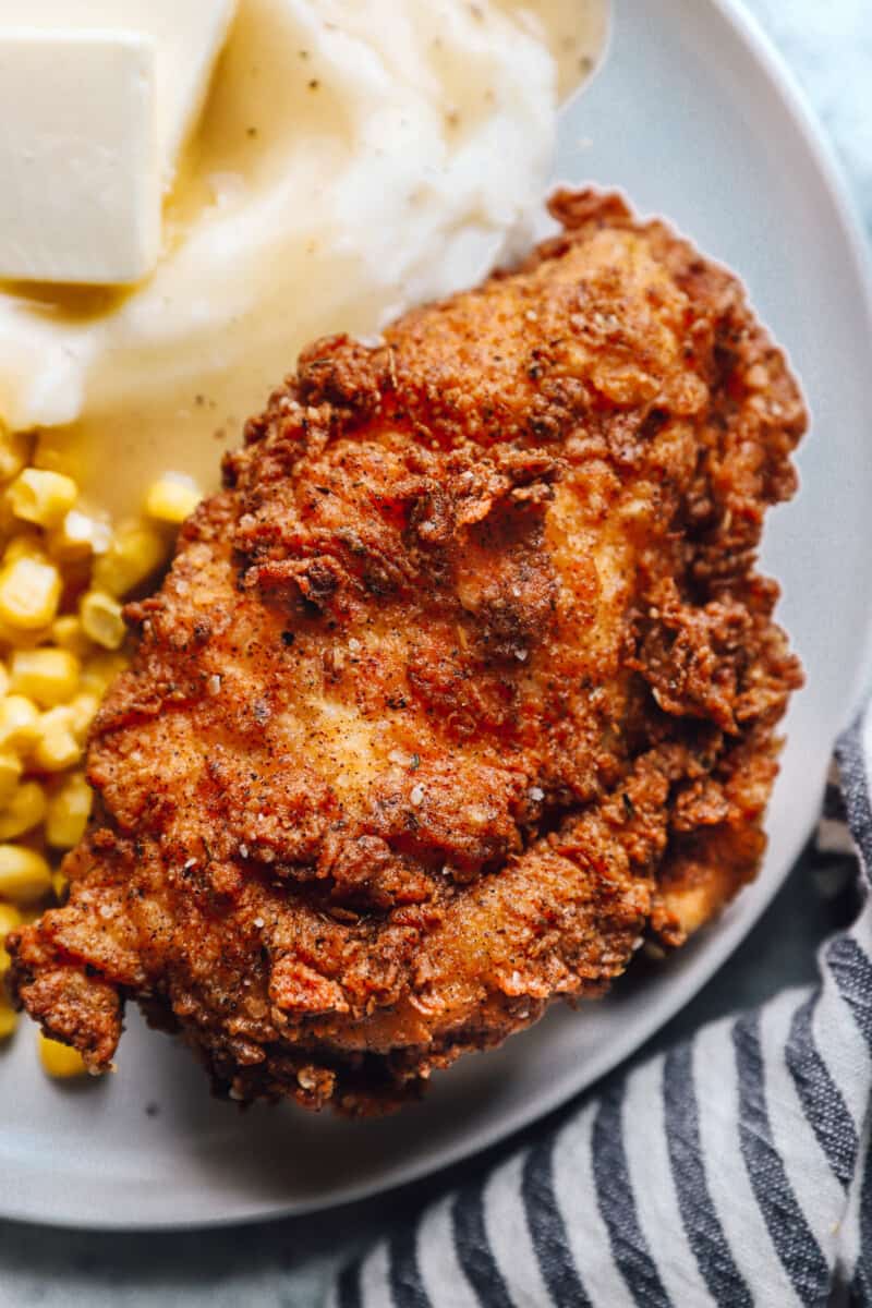 close up view of a piece of kentucky fried chicken on a white plate with corn and mashed potatoes.