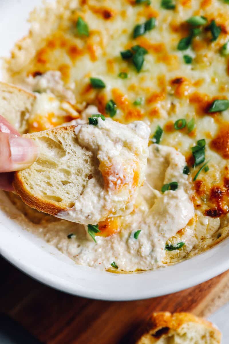 dipping a piece of bread into cheesy crab dip