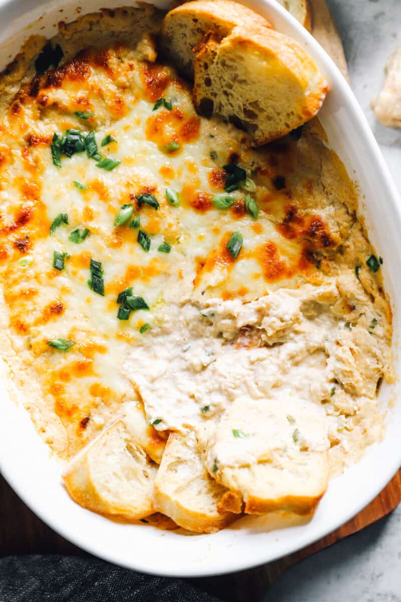 hot crab dip in a baking dish with pieces of bread dipped in