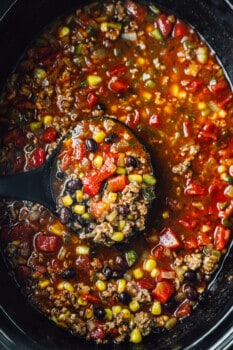overhead view of a ladle scooping taco soup from a crockpot.