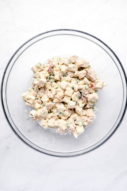 cubed chicken added to ingredients for bacon ranch chicken salad in a glass bowl.