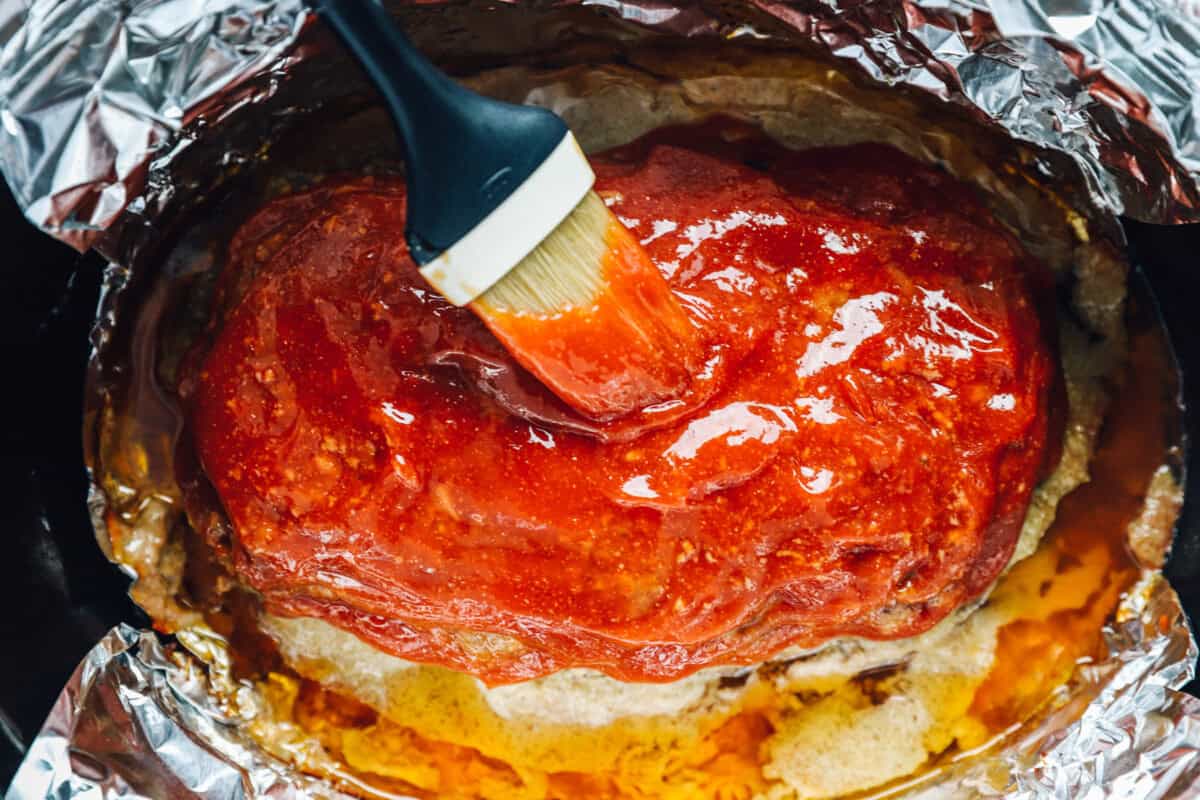 overhead view of glaze being brushed onto crockpot meatloaf in a slow cooker.