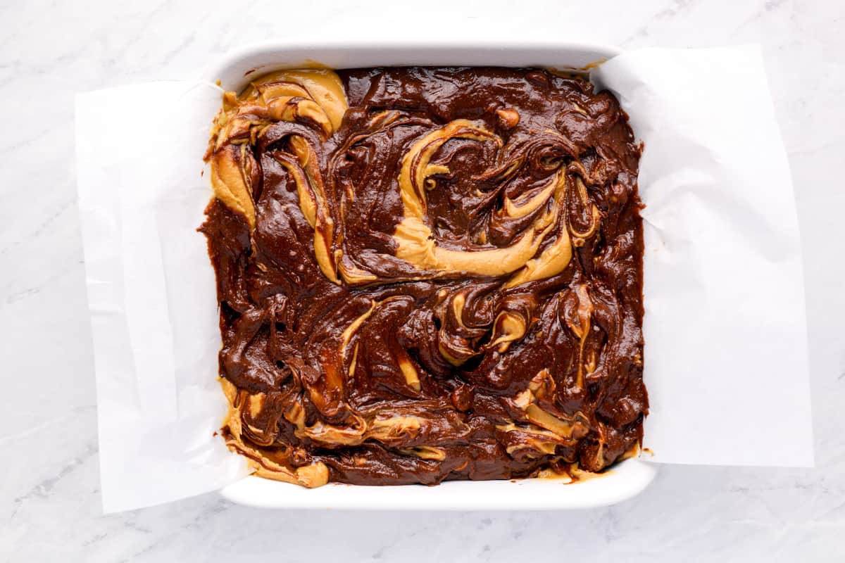 Overhead view of swirled peanut butter brownie batter in a square baking pan.