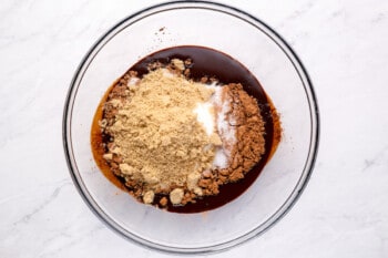 overhead view of cocoa powder, sugar, and brown sugar added to melted chocolate in a glass bowl.