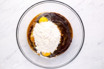 overhead view of eggs, vanilla, espresso powder, flour, and salt added to peanut butter brownie batter in a glass bowl.