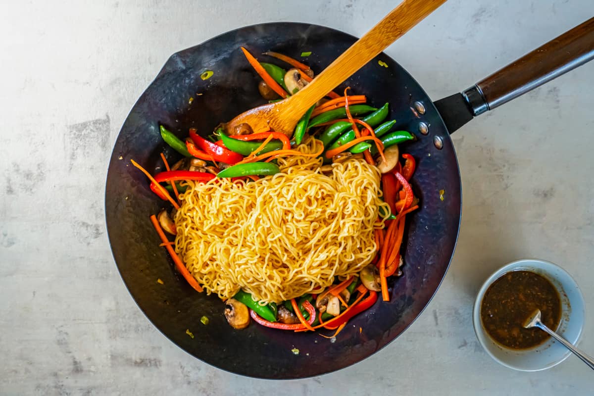 lo mein noodles added to vegetables in a wok.