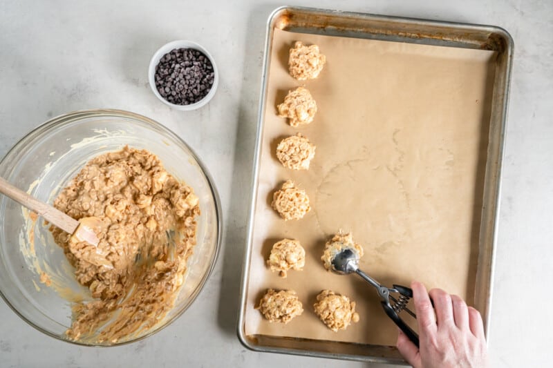 a hand using a cookie scoop to scoop avalanche cookies onto a baking sheet.