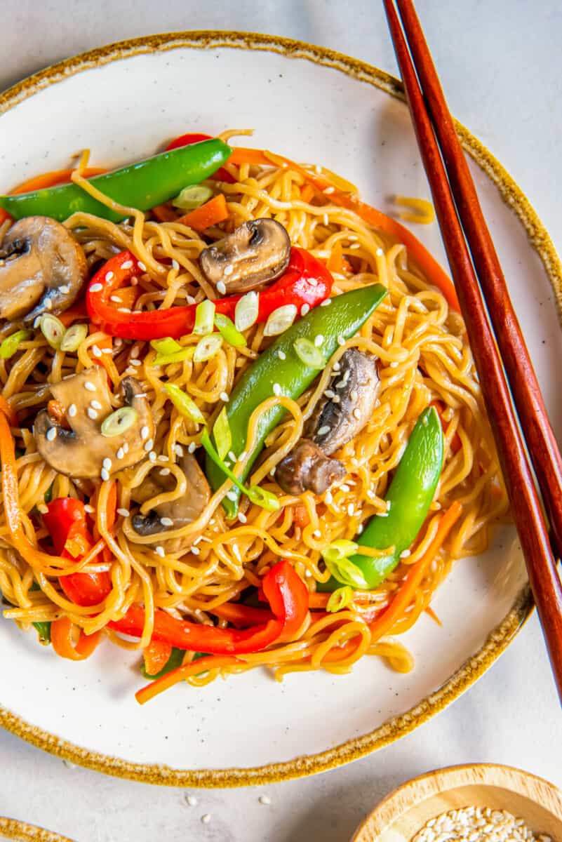 overhead view of vegetable lo mein on a white plate with chopsticks.