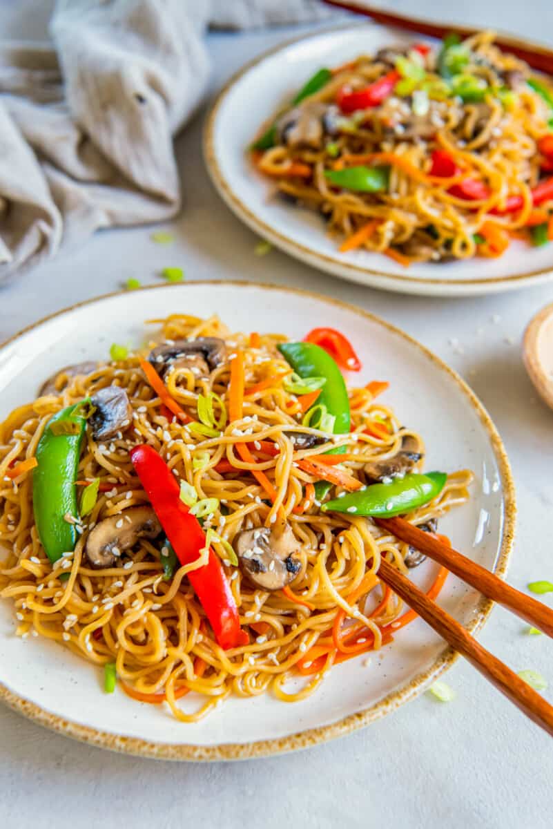 vegetable lo mein on white plates with chopsticks.
