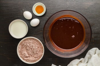 a bowl of chocolate sauce, eggs, flour and other ingredients on a wooden table.