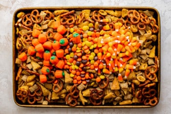 mini pretzels, bugles, Chex, candy corn, candy pumpkins, and Reese's pieces piled up in a baking tray
