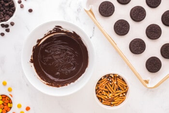 bowls of melted chocolate and pretzel sticks next to a tray of Oreos