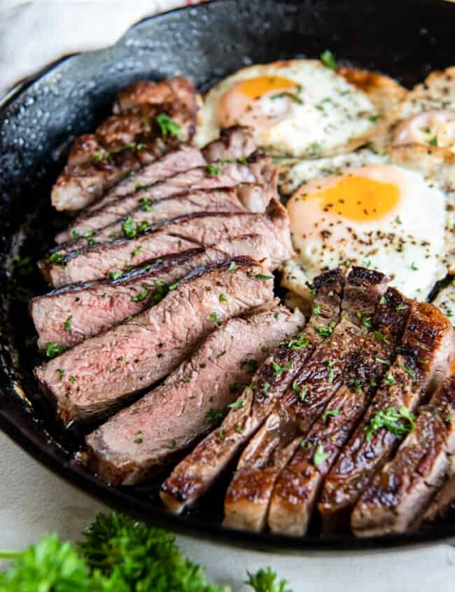 close up view of steak and eggs in a cast iron pan.