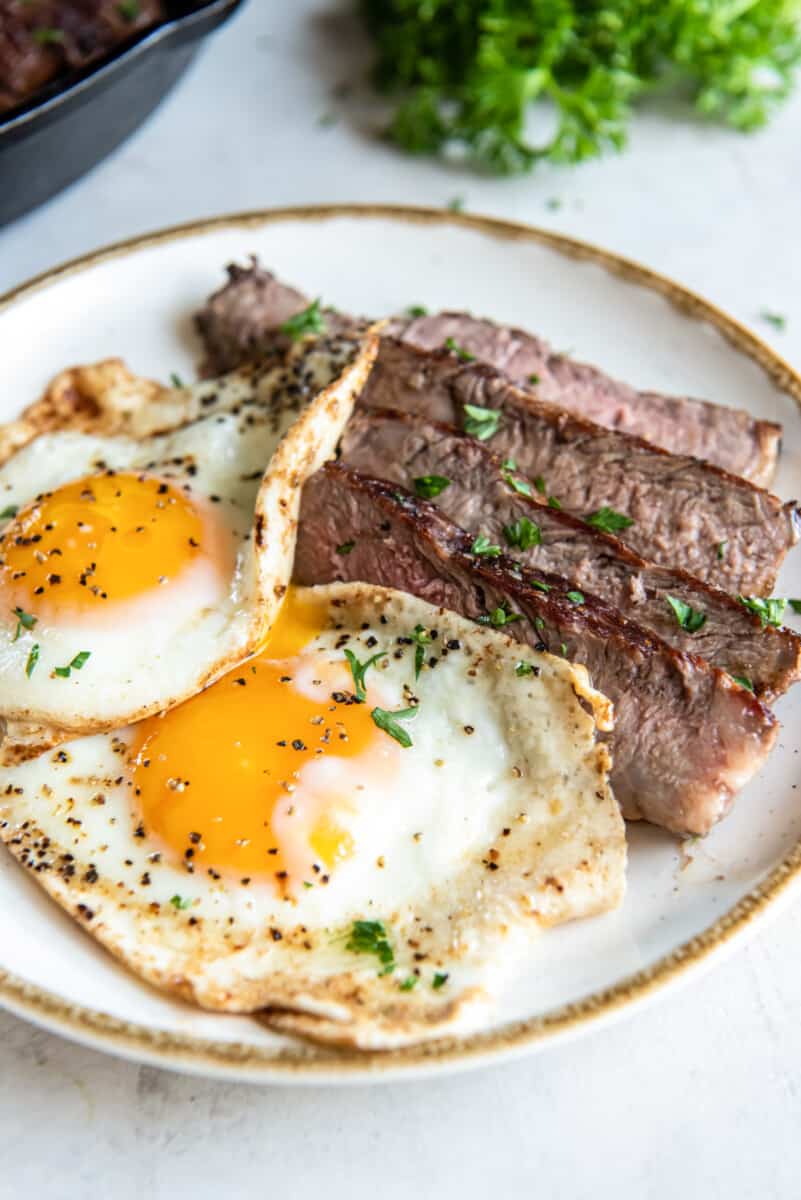 sliced steak and 2 fried eggs on a white plate.