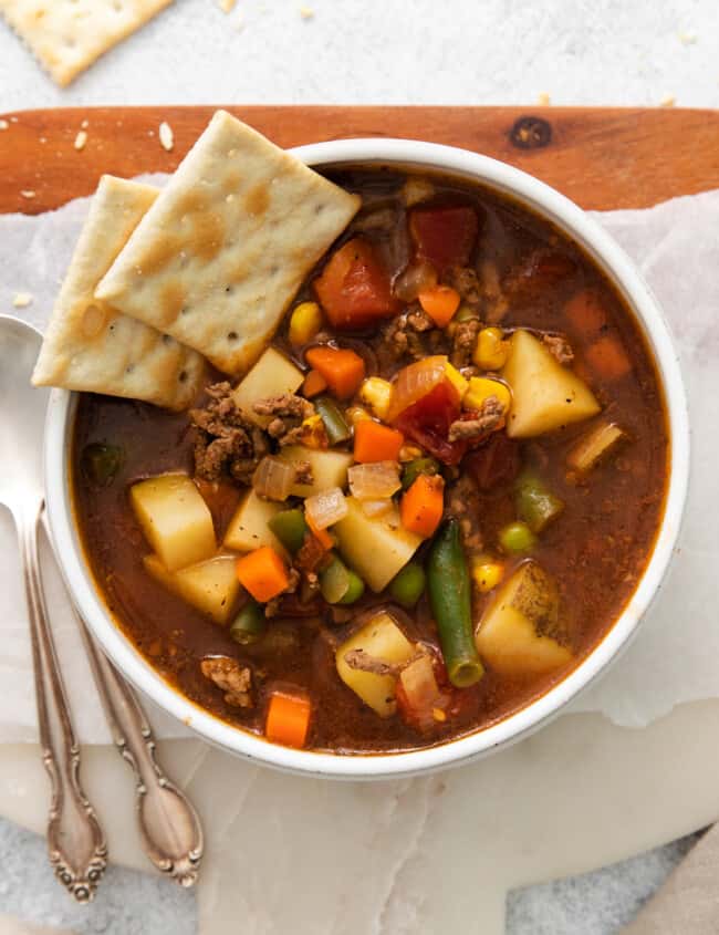 overhead view of hamburger soup in a white bowl with saltine crackers.