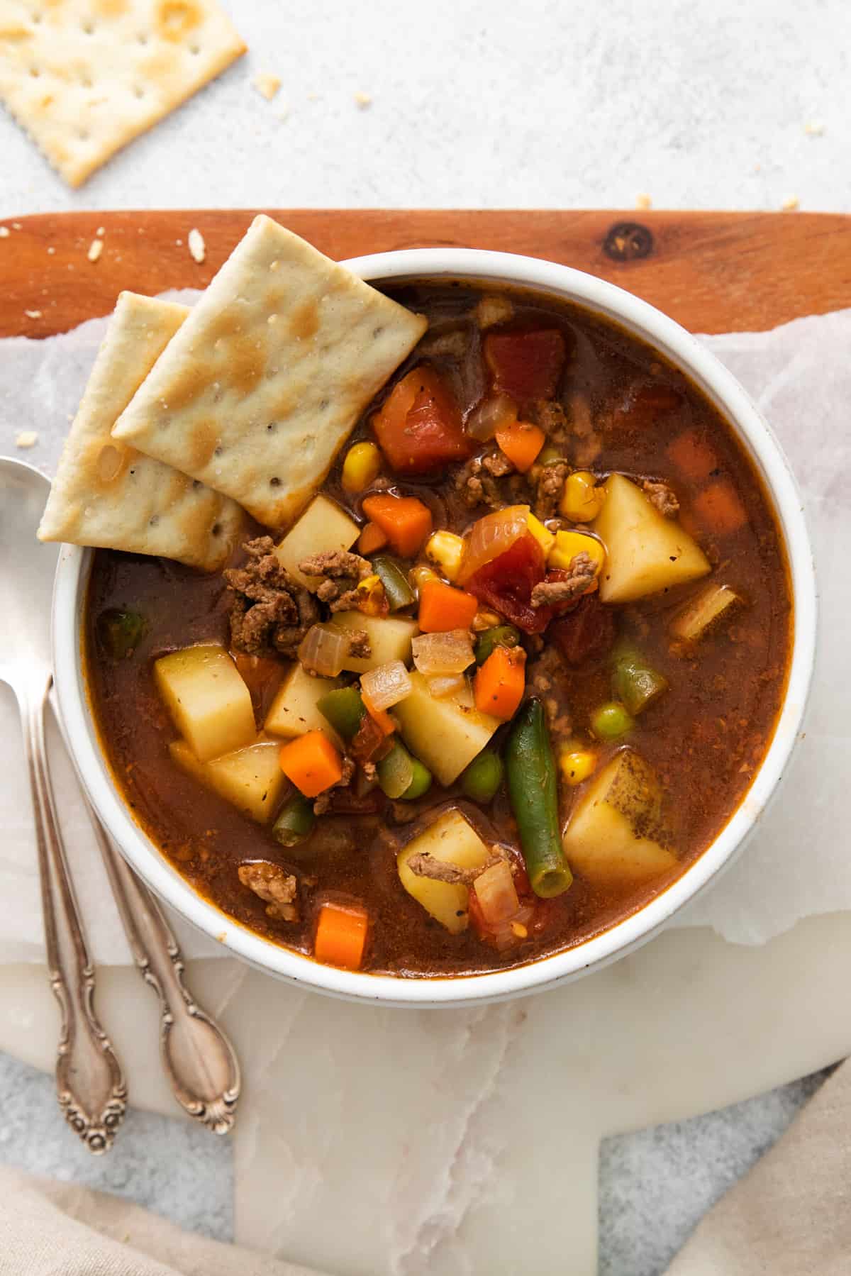 overhead view of hamburger soup in a white bowl with saltine crackers.