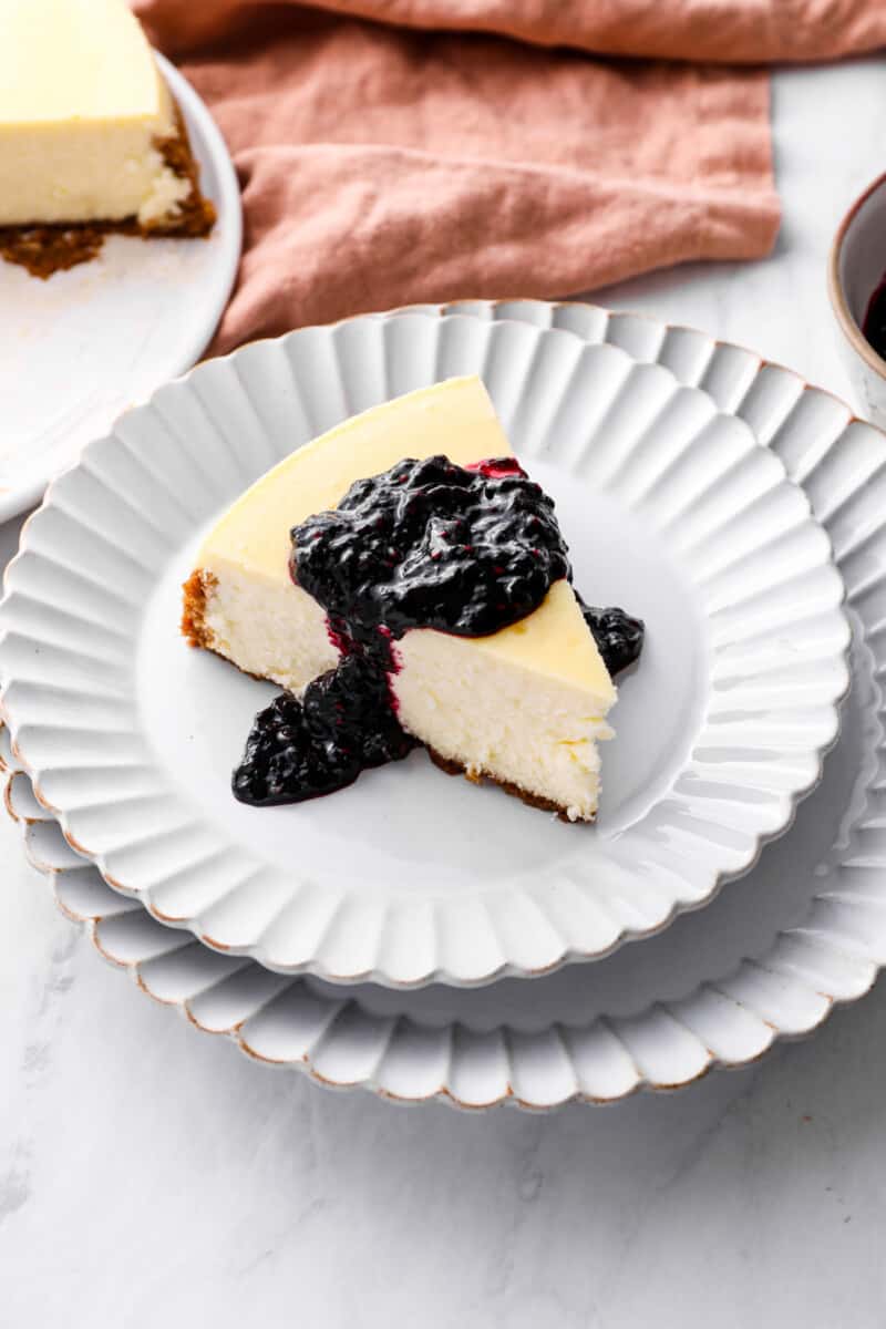 a slice of New York cheesecake on white plate, topped with blueberry sauce