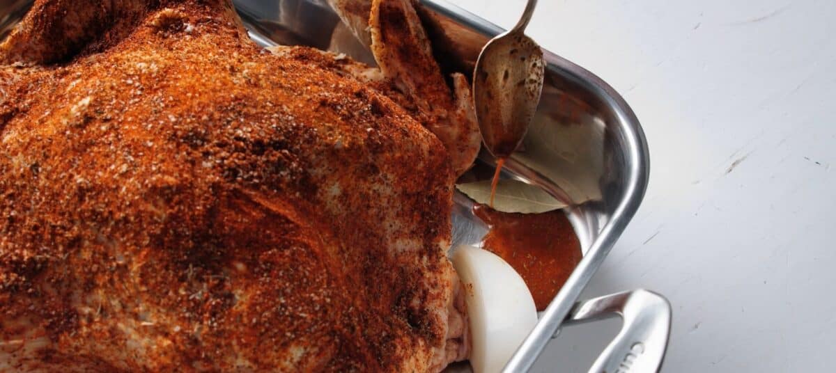 Seasoned turkey in a dish with an onion and bay leaf.